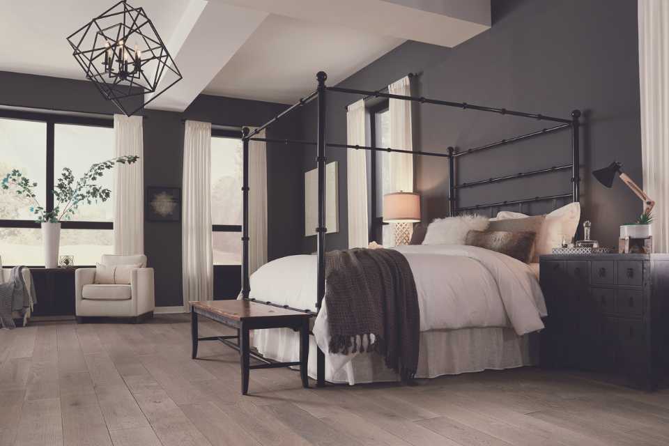 gray hardwood in gray cozy bedroom with greenery, fuzzy throw and fun lighting